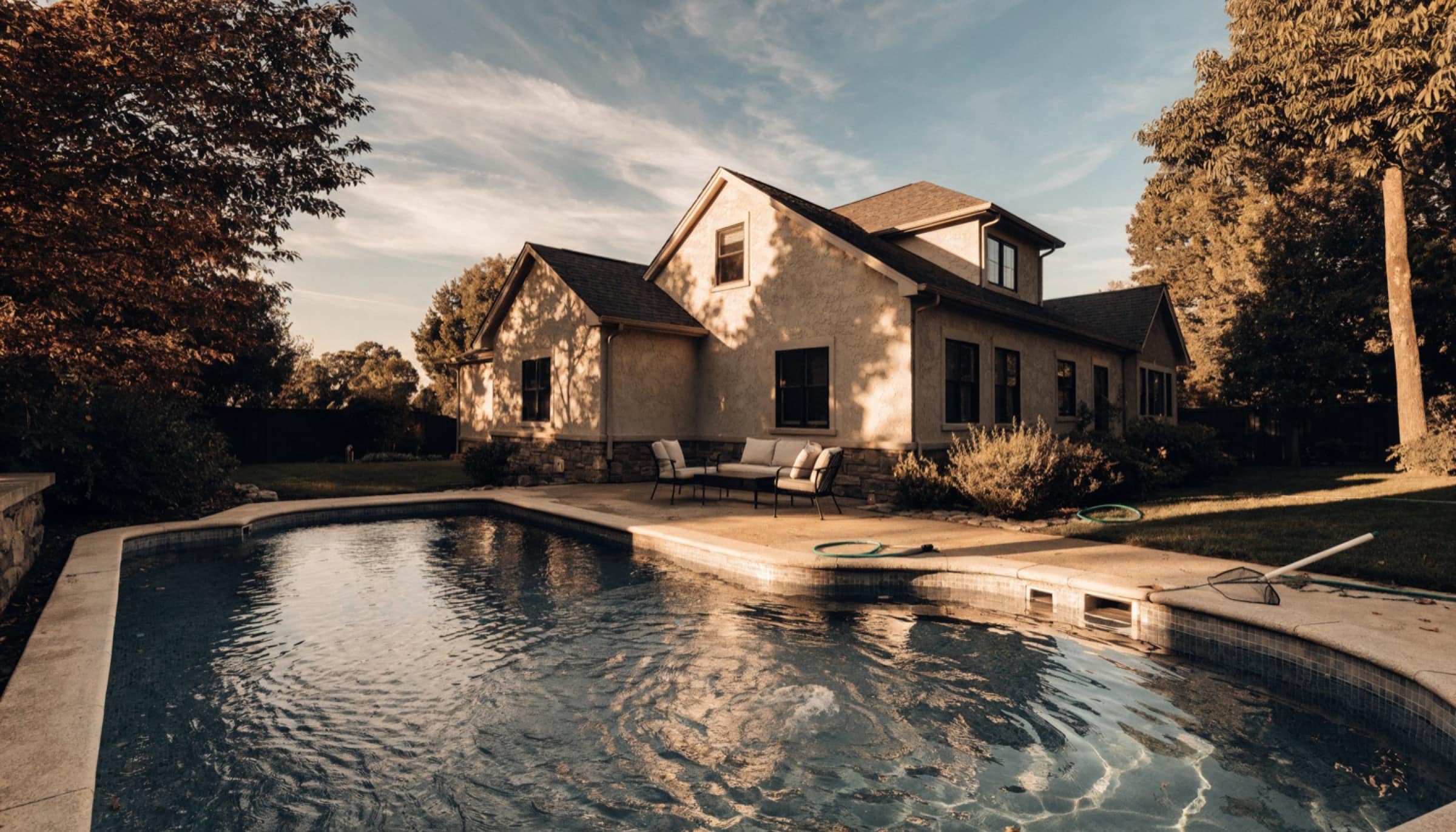 A contemporary luxury home at dusk, its windows lit warmly, reflected in a still swimming pool