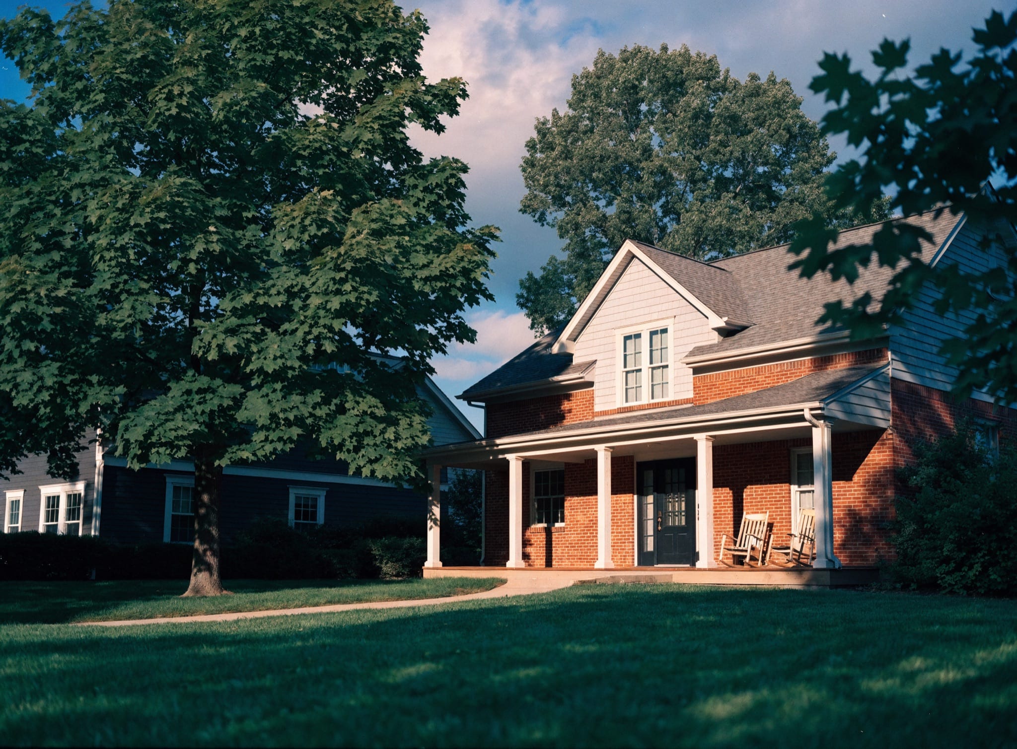 An established red-brick family home with a covered porch under a mature maple in late-morning sun