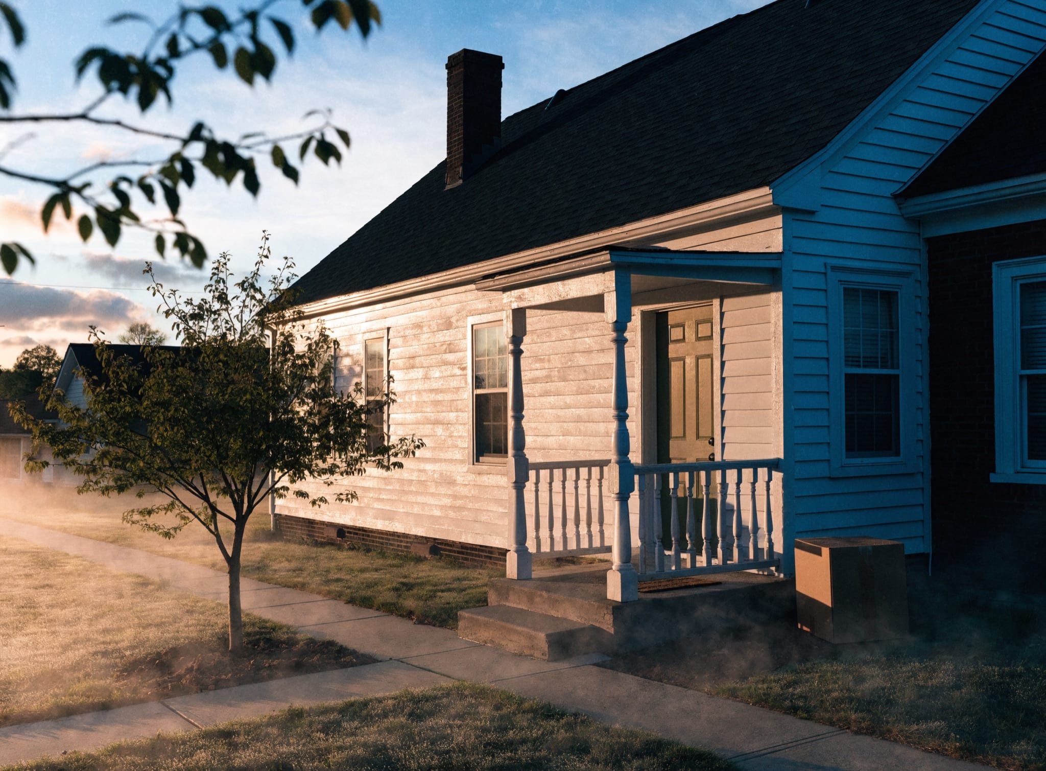 A modest American home at sunrise with a freshly painted front door and a newly planted tree