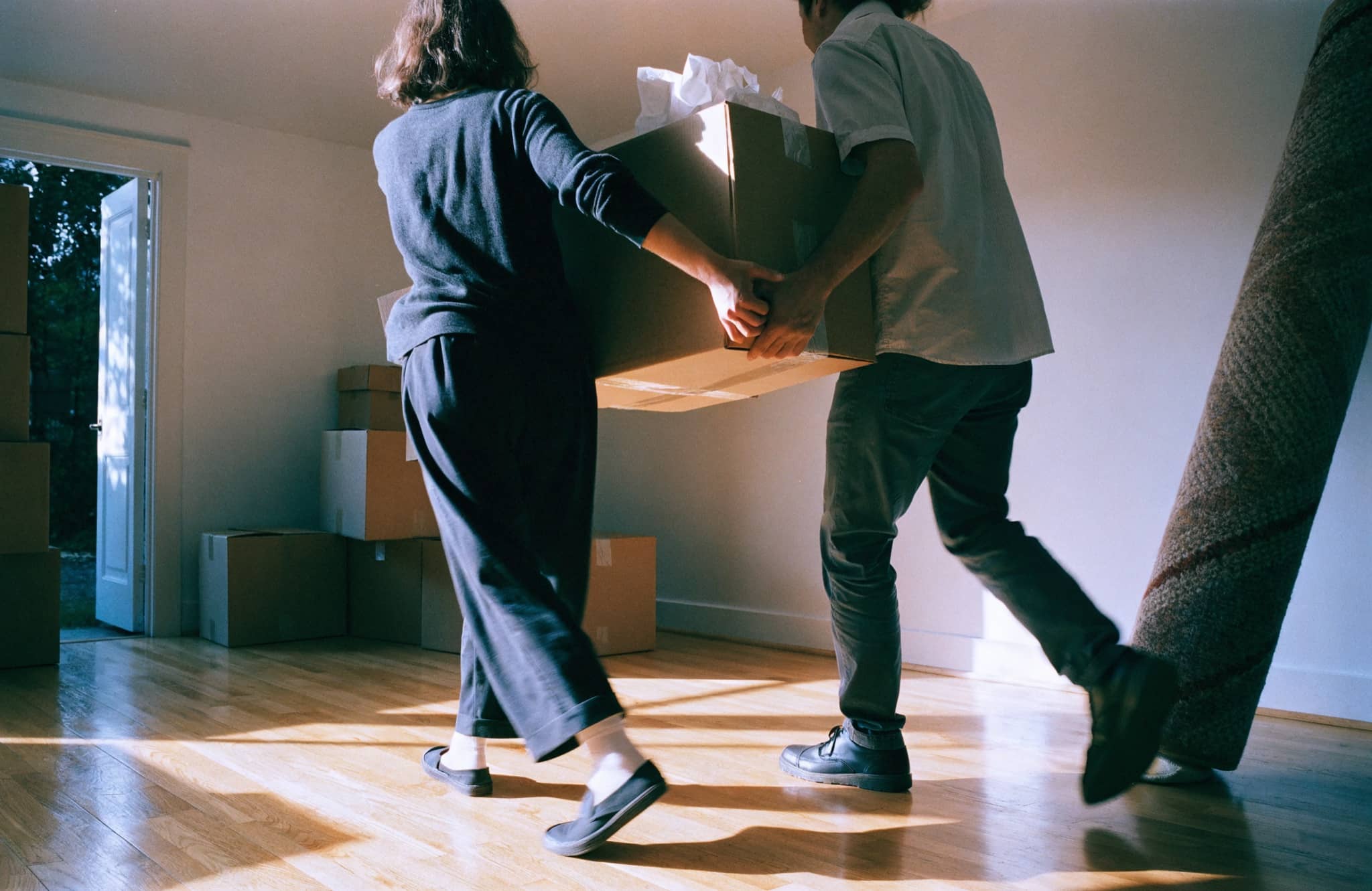 A couple standing in the sunlit empty living room of a home they have just bought, moving boxes stacked nearby